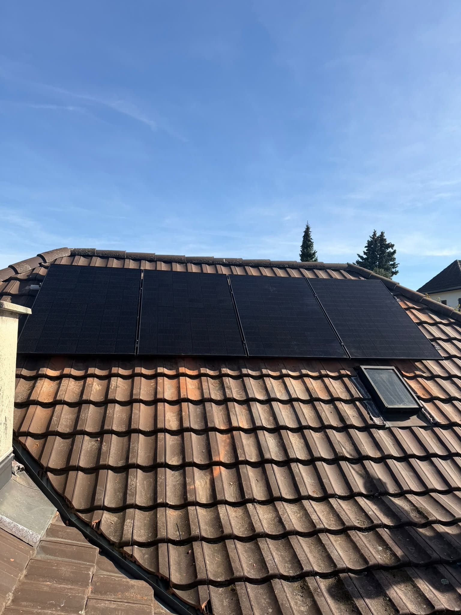 Vier schwarze Solarmodule in einer Reihe auf einem Ziegeldach, darunter ein Dachfenster